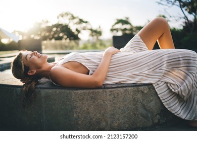 Side view of young woman lying and resting on swimming pool edge of resort hotel. Tourism, vacation and weekend. Joyful caucasian girl. Sunset time. Idyllic and tranquil lifestyle on Bali island