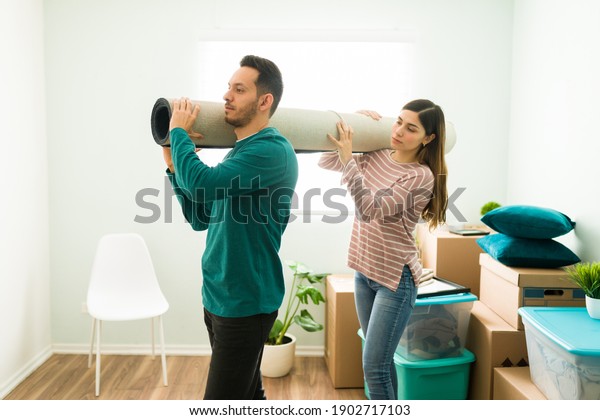 Side view of a young woman and man holding a\
rolled carpet together. Boyfriend and girlfriend carrying a rug to\
put on their new bedroom