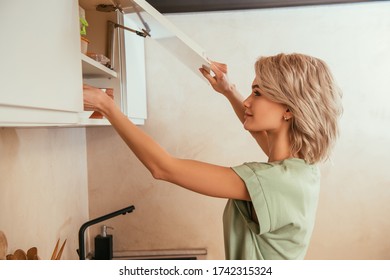 Side View Of Young Woman Opening Door Of Kitchen Cabinet