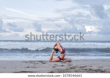 side view of young woman practicing yoga in One Legged King Pigeon pose (Eka Pada Rajakapotasana) on seashore