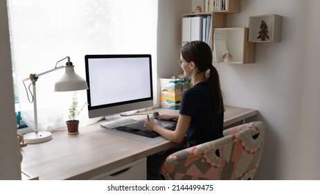 Side view young woman, professional designer working sit at table with PC white mock up screen, makes retouch, use editing application, busy in creative task use digital graphic tablet and drawing pen