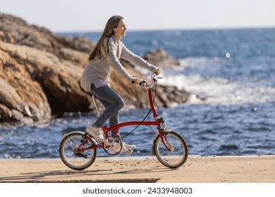 Side view of young woman riding an urban bicycle by the sea - Powered by Shutterstock