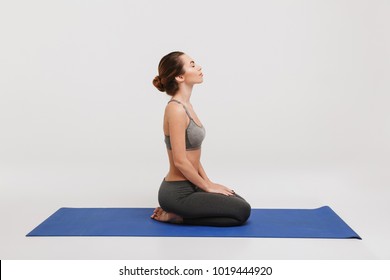 Side View Of Young Woman Sitting On Yoga Mat Isolated On White