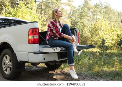 Side View Of Young Woman Sitting In Trunk Of Pick Up Car Outdoors 