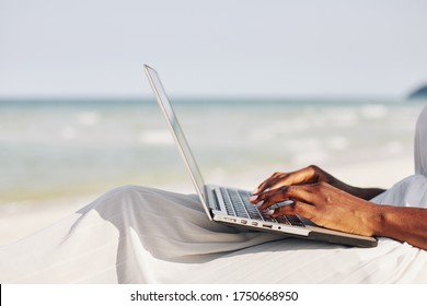 Side view of young woman sitting on beach and typing on laptop