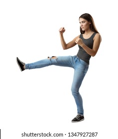 Side View Of Young Woman In Sleeveless Top And Jeans With Right Leg Kicking Forward And Arms In Fighting Position Isolated On White Background. Wake Up Your Fighting Spirit. Train Body. Learn To Fight