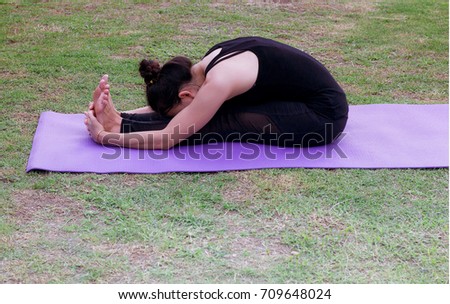 Side view Young woman stretching exercise outdoors.  is sitting forward bending on the lawn her hands are holding the feets.healthy lifestyle Concept,
