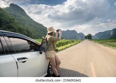 side view of young woman traveler taking pictures of mountains in the sky on the road beside the car