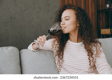 Side view young woman wear casual clothes sits on grey sofa couch look aside prop up chin drinking wine stay at home hotel flat rest relax spend free spare time in living room indoor. Lounge concept - Shutterstock ID 2367234531