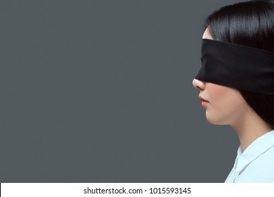 side view of young woman wearing black blindfold isolated on grey 