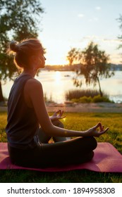 Side view of a young woman wearing sport clothes practicing yoga, sitting in lotus pose and meditating on the background of nature. Wellbeing and healthy lifestyle concept