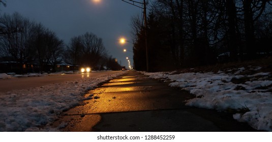 Side Walk With Reflection From Street Lights. Car In The Distance With Low Angle Shot. Snow On The Side Of Side Walk.