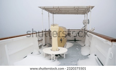 Side wing of large cargo vessel with gyro repeater and navigational console full of snow during passing of Pacific ocean winter time