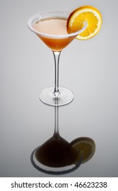 Sidecar Mixed Drink With Orange Garnish And Sugar Rim On Plain Grey Background