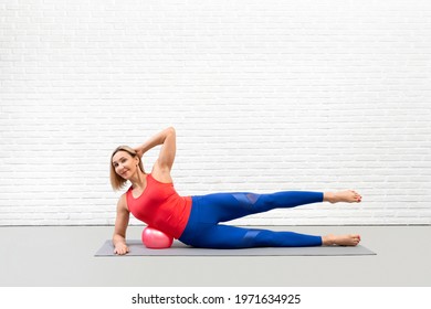 Side-lying leg circles drill. Fit adult smiling woman practice pilates using a small fit-ball ind