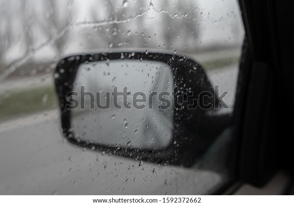 sideview car mirror in rain weather,\
blurred reflection in the mirror. Road travel\
concept.