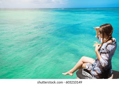 Sideview Of Cheerful Woman In Fashion Beach Look Sitting On Pier Admiring Fantastic Ocean