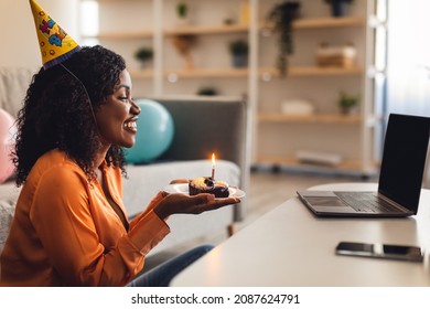Side-View Of Happy Black Female At Laptop Holding Birthday Cake With Candle Video Calling Having Remote Celebration At Home. Online B-Day Party Concept