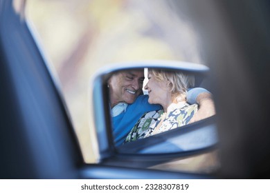 Side-view mirror reflection of couple hugging inside car