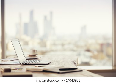 Sideview of office desktop with blank laptop and various office tools on blurry Moscow city background