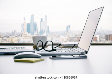 Sideview Of Office Table With Laptop, Glasses And Other Items On Moscow City Background