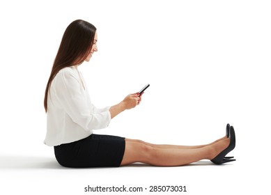 Sideview Photo Of Woman In Formal Wear Sitting On The Floor And Using Her Smartphone. Isolated On White Background