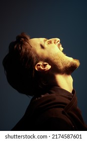 Sideview Portrait Of A Bearded Brunet Man Screaming From Pain. Studio Portrait On A Dark Blue Background. People And Emotions.