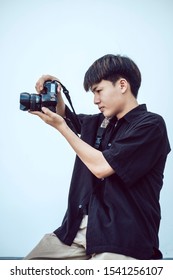 Sideview Portrait Of Cool Asian Guy Holding Camera On White Background In Studio.