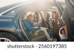 Side-view portrait of pretty caring mom fastening belts of little little girl sitting in baby car seat with older brother smiling and talking to dad. Preparation for family car trip.