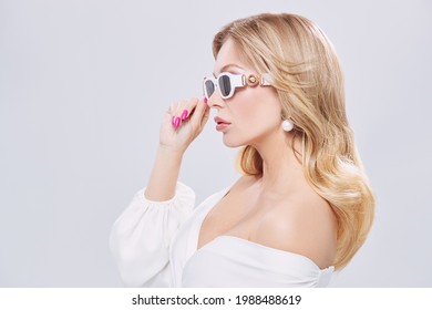 Sideview Portrait Of A Stylish Sexy Middle Aged Woman In A White Dress, Precious Jewelry And Sunglasses On A White Background. Beauty, Fashion. Copy Space.