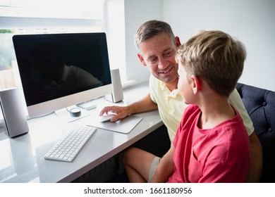 A side-view shot of a father and son sitting down using a computer, they are learning together.