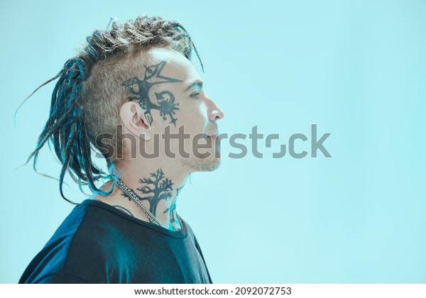 Sideview shot of a\
handsome  punk rock musician with dreadlocks and tattoos in black\
T-shirt smiling and looking away. Blue studio background. Youth\
alternative culture. Punk\
rock.