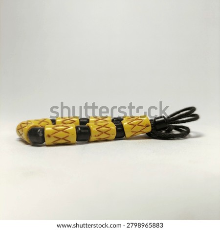 A side-view studio macro shot of an ethnic tribal bracelet laid horizontally on a clean white background. The piece is composed of cylindrical yellow beads engraved with geometric red criss-cross patterns, neatly alternating with smooth, glossy black spacer beads on an adjustable dark woven fiber cord.