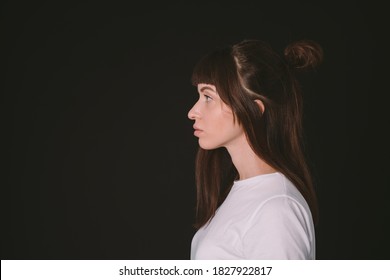 Sideview Studio Portrait Of A Pretty Brunette Woman In A White Blank T-shirt, Against A Plain Black Background, Looking To The Side