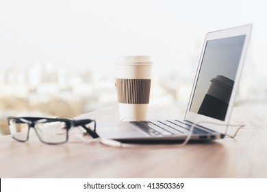 Sideview Of Wooden Desk With Glasses, Laptop, Coffee Cup And Headphones On Blurry Background