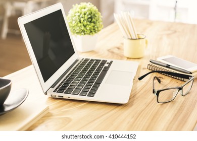 Sideview Of Wooden Office Desktop With Blank Laptop, Glasses, Plant And Other Items