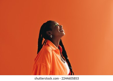 Sideview of a young black woman smiling in a studio. Woman with makeup standing against an orange background.