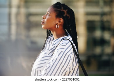 Sideview of a young businesswoman looking thoughtful while standing outdoors in the city. Young black business woman commuting to work in the morning.