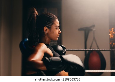 Sideview Of A Young Female Boxer Leaning Against The Ropes In Boxing Ring. Confident Female Athlete Getting Ready For A Boxing Match.