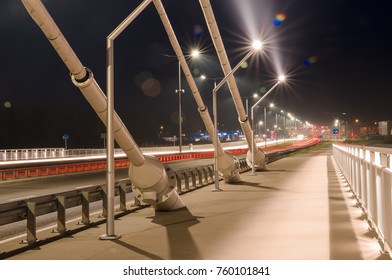 sidewalk and highway going through a cable-stayed bridge with big steel cables, closeup at night time in bright lights