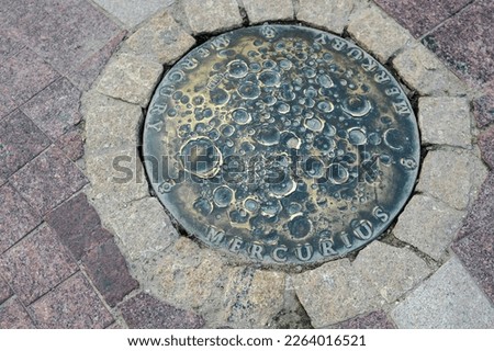 sidewalk metal manhole cover with the image of mercury, city sidewalk gutter system.