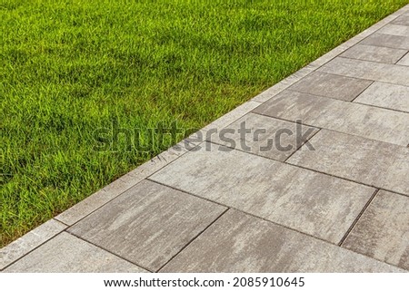 The sidewalk paved with large slabs is separated from the mowed lawn by a curb. Selective focusing.