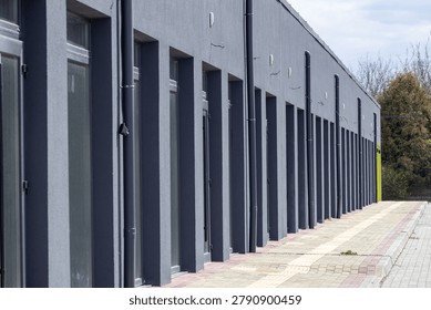 Sidewalks next to gray storefronts stretch along the street as trees are visible in the background on a clear day with few clouds.
