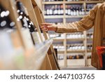 Sideways close up young customer woman wear casual clothes choosing alcohol wine bottle shopping at supermaket store grocery shop buying products inside hypermarket. Purchasing food gastronomy concept