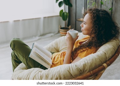 Sideways top view calm young woman wear t-shirt drink coffee read book sits in armchair stay at home flat rest relax spend free spare time in living room indoor grey wall - Powered by Shutterstock