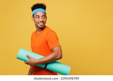 Sideways young fitness trainer sporty man sportsman wear orange t-shirt hold in hand yoga mat look aside area spend time in home gym isolated on plain yellow background. Workout sport fit abs concept - Shutterstock ID 2396398789