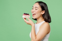 Sideways Young Happy Fun Woman Wear White Clothes Holding In Hand Bite Pice Of Cake Dessert Isolated On Plain Pastel Light Green Background. Proper Nutrition Healthy Fast Food Unhealthy Choice Concept