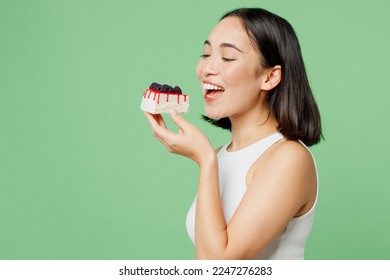 Sideways young happy fun woman wear white clothes holding in hand bite pice of cake dessert isolated on plain pastel light green background. Proper nutrition healthy fast food unhealthy choice concept - Powered by Shutterstock