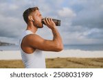 Sideways young strong athletic toned fit sportsman man he wear sports clothes earphones drink protein shake warm up train at sunrise sun dawn over sea beach outdoor on seaside in summer day morning.