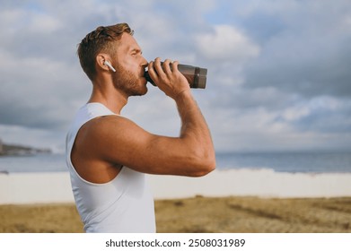 Sideways young strong athletic toned fit sportsman man he wear sports clothes earphones drink protein shake warm up train at sunrise sun dawn over sea beach outdoor on seaside in summer day morning. - Powered by Shutterstock